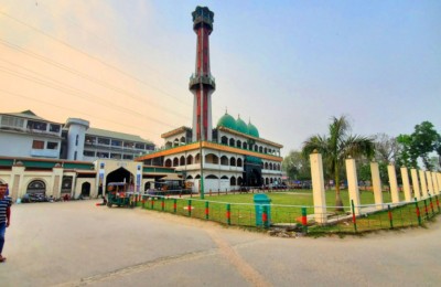 A view of a large mosque complex with tall minaret and landscaped entrance at sunset.
