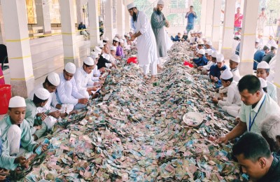A massive heap of mixed currency notes being sorted by rows of people inside the mosque premises.