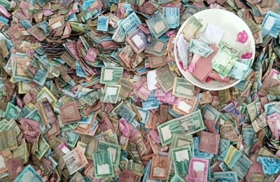 A close-up of heaps of colorful banknotes with a white plate holding coins on top.