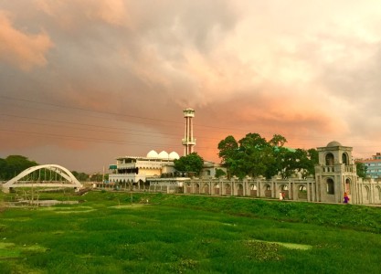 A wide landscape showing the mosque and bridge under a dramatic evening sky.