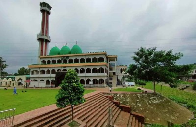 A daytime scene showing the mosque with lush lawns, trees, and walking paths.